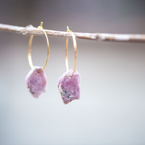 Peut inclure: Une paire de boucles d'oreilles cr&eacute;oles en or avec des accents de pierres roses. Les boucles d'oreilles sont suspendues &agrave; une branche.