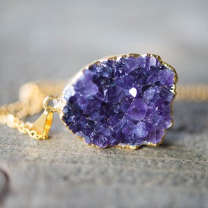 May include: A gold chain necklace with a purple amethyst crystal pendant. The crystal is a cluster of small, faceted stones.