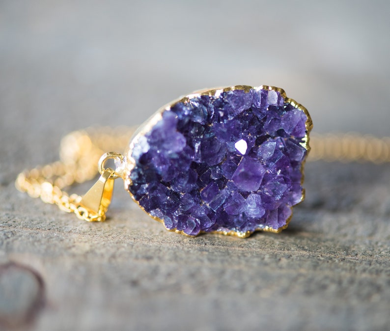 May include: A gold chain necklace with a purple amethyst crystal pendant. The crystal is a cluster of small, faceted stones.
