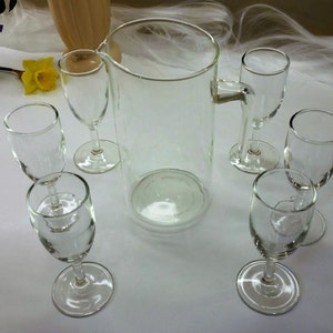 May include: A set of six clear glass drinking glasses, including a pitcher, on a white surface.