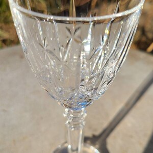 May include: A clear glass stemmed shot glass with a cut crystal design. The glass is empty and sitting on a gray surface.
