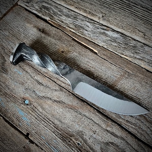 May include: A hand-forged knife with a twisted metal handle and a sharp, silver blade. The knife is resting on a weathered wooden surface.