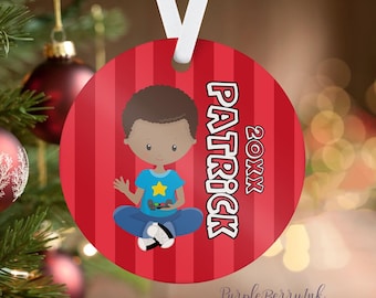 Könnte beinhalten: Runder Weihnachtsbaumschmuck mit rot-weiß gestreiftem Hintergrund. Er zeigt einen Cartoon-Jungen in einem blauen Hemd und Jeans, der einen Gamecontroller hält. Der Name "PATRICK" und das Jahr "20XX" sind aufgedruckt. Ein weißes Band ist befestigt.