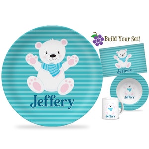 May include: A personalized children's dinnerware set featuring a white polar bear wearing a blue scarf on a turquoise and white striped background. The set includes a plate, bowl, and mug, all with the name "Jeffery" printed on them.