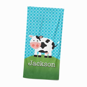 May include: A blue and green beach towel with a white cow and the name "Jackson" printed on it.