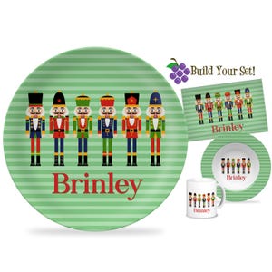 May include: A green and white striped plate, bowl, mug, and placemat set featuring colorful nutcracker soldier illustrations. The word "Brinley" is printed in red on the plate and other items. The set is designed for building a complete collection.