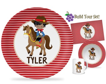May include: A red and white striped plate with a cartoon cowboy riding a horse. The plate has the name "TYLER" printed on it.  The plate is part of a set that includes a bowl, a mug, and a placemat.  Build Your Set!