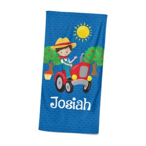 May include: A blue beach towel with a cartoon illustration of a boy driving a red tractor in an apple orchard. The sun is shining and the towel is personalized with the name "Josiah".