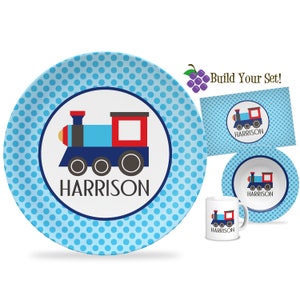 May include: Blue and red train design on a blue polka dot dinner plate with the name Harrison.  The set includes a matching bowl, mug, and placemat.