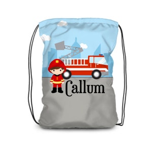 May include: A red fire truck with a ladder and a firefighter in front of a blue and white cityscape. The bag is gray with the name Callum printed on it.