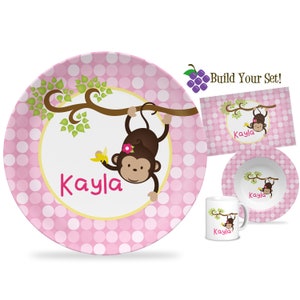 May include: Pink polka dot children's dinnerware set with a monkey hanging from a tree branch. The set includes a plate, bowl, and mug. The name "Kayla" is personalized on each piece.