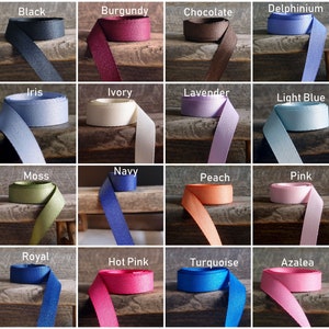 May include: A collection of 24 different colored ribbon spools, each with a label indicating its color. The colors include baby maize, black, burgundy, chocolate, delphinium, gold, hunter, iris, ivory, lavender, light blue, light gold, lime, moss, navy, peach, pink, purple, red, royal, hot pink, turquoise, azalea, and silver.