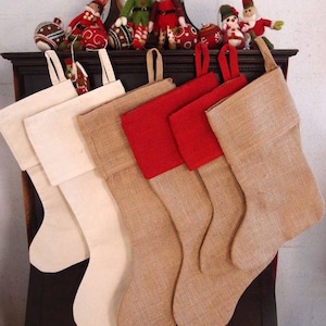 May include: Four Christmas stockings, two are made of burlap with red felt trim and two are made of white canvas. The stockings are hanging on a wooden mantel.