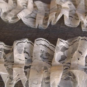 May include: White lace trim with a ruffled design. The lace is delicate and has a vintage look.