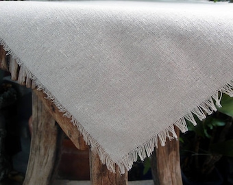 May include: A white linen table runner with a frayed edge. The runner is laying on a rustic wooden table.