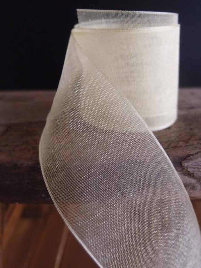 May include: A roll of sheer, ivory-colored ribbon. The ribbon has a delicate, open weave, and a subtle sheen. The spool is partially unrolled, revealing the texture and depth of the material. The ribbon is suitable for crafts, gift wrapping, or decorative purposes.