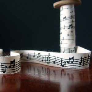 May include: A spool of white ribbon with black musical notes printed on it. The ribbon is unraveled and the spool is sitting on a wooden surface.