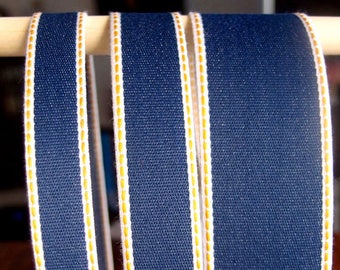 Può includere: Tre bobine di nastro blu navy con cuciture bianche e dorate. Il nastro è tessuto e ha una superficie testurizzata.