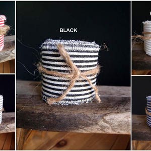 May include: Assortment of striped fabric ribbon rolls in various colors, including red, white, black, gray, and blue. Each roll is tied with twine and has a frayed edge.