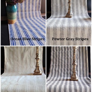May include: Four fabric table runners with vertical stripe patterns in ocean blue, pewter gray, white, and solid pewter gray. Each runner is labeled with its color and pattern. A decorative candlestick is on some of the runners.