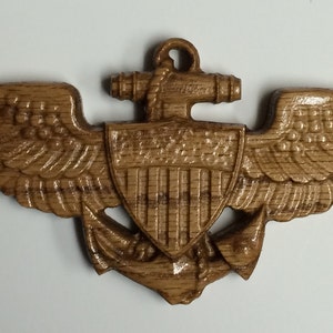 May include: A wooden Naval Aviator Wings pin with a carved anchor and shield with the words "United States" on it.
