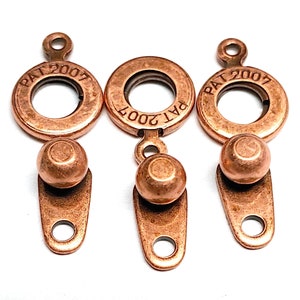 May include: Three copper-colored metal clasps with a round ring and a ball on the bottom. Each clasp has the text "PAT 2007" engraved on the ring.