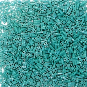 May include: A large quantity of turquoise blue glass beads with two holes in each bead. The beads are shaped like small rectangles with rounded edges.