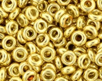 May include: A close-up image of a large quantity of gold-colored metal beads. The beads are small and round with a hole in the center. They are arranged in a random pattern.