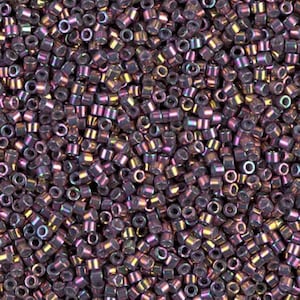 May include: A close-up view of a pile of small, cylindrical beads. The beads are a dark purple color with iridescent highlights of pink, gold, and green. The beads are tightly packed together, creating a textured surface. These beads are suitable for jewelry making and crafts.