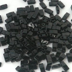 May include: A pile of black rectangular seed beads with two holes in each bead.