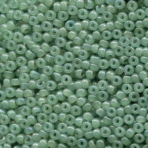 May include: Close-up of a pile of small, round, translucent beads in a pale green color. The beads have a hole through the center and are densely packed together, creating a textured surface. Ideal for jewelry making and crafts.