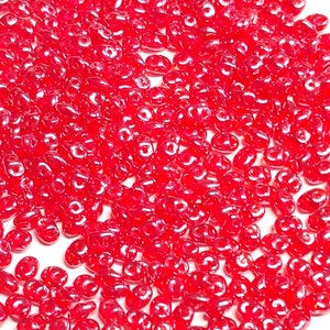 May include: A large pile of small, red, glass seed beads. The beads are oval shaped and have a glossy finish.