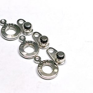 May include: Four silver metal clasps with a round ring and a dome-shaped top. Each clasp has the text "PAT. 2007" engraved on the ring.