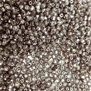 May include: A close-up image of a large quantity of small, faceted, silver-colored beads. The beads are arranged in a random pattern, creating a shimmering, reflective surface.
