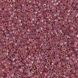May include: A close-up view of a pile of small, cylindrical beads. The beads are a translucent pink color with a reddish-pink center. The beads are scattered, creating a textured surface.