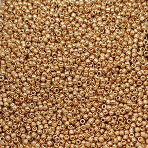 May include: A close-up view of a large quantity of small, round, gold-colored beads. The beads are arranged in a random pattern, creating a textured surface.