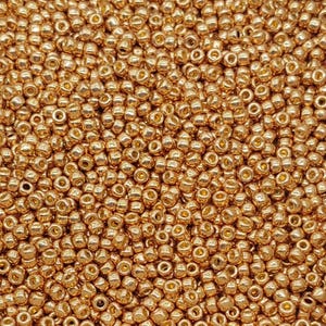 May include: A close-up view of a large quantity of small, round, gold-colored beads. The beads have a metallic sheen and are arranged in a random pattern.