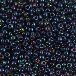 May include: Close-up of a pile of iridescent seed beads. The beads are a mix of dark blue, purple, and green, with a shiny, metallic finish. These small, round beads are used for jewelry making and crafts.