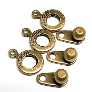 May include: Four antique gold-toned metal clasps with a round ring and a ball on a flat piece. The rings are engraved with "PAT 2007".