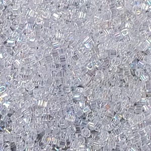 May include: A close-up image of a large quantity of small, clear iridescent glass beads. The beads are all the same size and shape, and they are arranged in a random pattern.