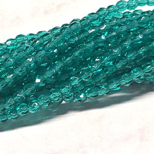 May include: A strand of teal blue faceted glass beads. The beads are small and have a slightly irregular shape.