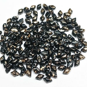 May include: A large quantity of black and gold glass beads in a diamond shape. The beads have a speckled gold finish.
