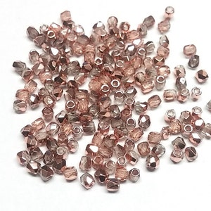 May include: A large pile of rose gold and clear glass beads. The beads are faceted and have a shiny finish.