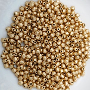 May include: A large pile of gold-colored faceted glass beads. The beads are small and have a matte finish.