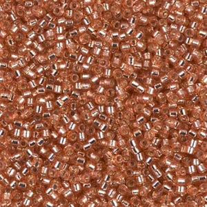 May include: Close-up of a pile of small, cylindrical beads in a warm, copper color. Each bead has a metallic silver lining, creating a reflective effect. The beads are densely packed, filling the frame.