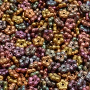 May include: A close-up shot of a pile of flower-shaped beads in various metallic colors. The beads are a mix of gold, bronze, purple, and teal, with a shiny, iridescent finish. Each bead has a hole in the center.