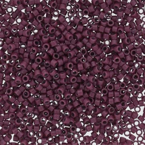 May include: Close-up of a pile of small, cylindrical beads in a deep burgundy color. Each bead has a hole running through the center. The beads are scattered, creating a textured surface.