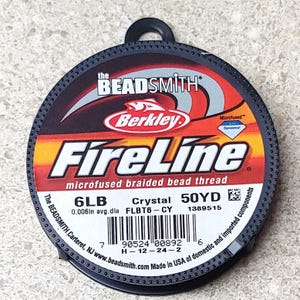 May include: A spool of Berkley FireLine Crystal microfused braided bead thread in a black container. The spool is labeled with the text "6LB 0.006in avg.dia Crystal FLBT6-CY 50YD 1389515".