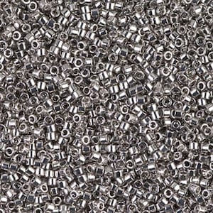 May include: A close-up view of a pile of small, shiny, silver-colored seed beads. The beads are cylindrical with a hole running through the center, reflecting light and creating a textured surface. These beads are commonly used for jewelry making and crafts.