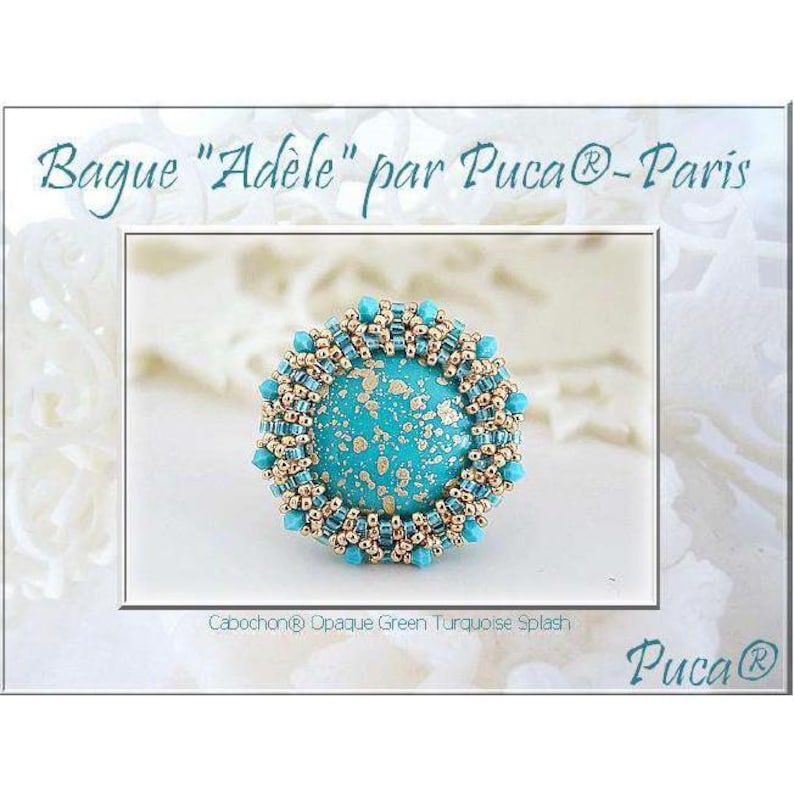 May include: A turquoise ring with a gold beaded border. The ring features a turquoise cabochon with a gold flecked design. The ring is labeled "Bague "Ad&egrave;le" par Pucca&reg; - Paris" and "Cabochon&reg; Opaque Green Turquoise Splash".